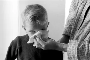 Boy in the 1950s. A mother holds a handkerchief over her sons nose as he blows his nose