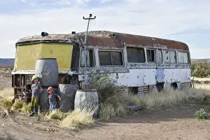 Boy and girl play at car wreck of an old bus