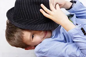 The boy half covers his face with a hat and smiles