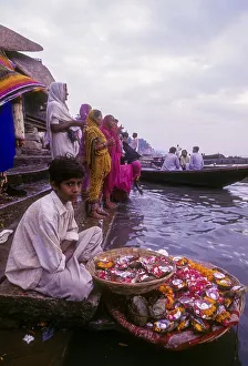 A boy selling mari gold flowers used in workship sitting in front of River Ganga Ganges at Varanasi Benaras