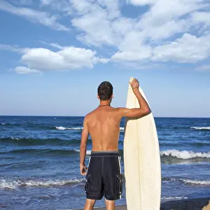 Boy surfer back rear view holding surfboard on blue beach