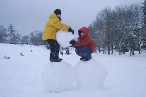 Two boys standing on big snoww balls
