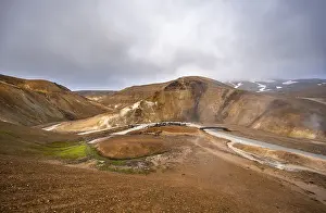 Bridge over steaming stream between colourful rhyolite mountains with snowfields