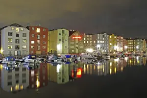 Brightly lit, different coloured houses reflected in the calm waters of the river Nidarelva