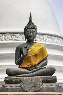 Bronze Buddha statue with yellow cloth in front of a white temple
