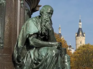 Bronze statue of a pensive man in front of a historic castle on an autumn day