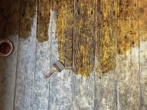 Brush placed on wooden floor in the process of being stained showing texture details