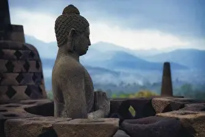 A Buddha statue sits carved in stone with mountains in the background