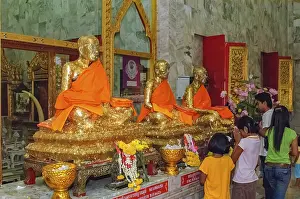 Buddhist believers Buddhists pray making offerings to statues of Buddhist monks covered with gold leaf at Wat Chalong