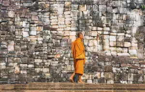 Buddhist monk walks in front of old stone wall