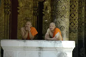 Buddhist monks leaning against a wall of Wat Mai Suwannaphumaham