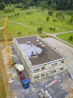Building shell with crane and workers on a construction site surrounded by green areas