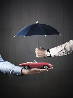 Businessman holding a small blue umbrella protecting a vintage car