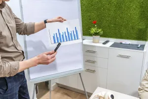 Businessman presenting bar chart on paper during a meeting in a modern coworking office with green wall