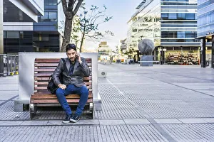 A businessman is talking on the cell phone while sitting on a bench in the street
