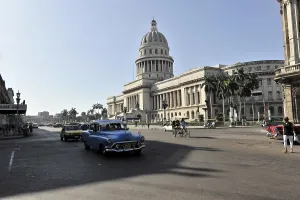A busy street in front of the Capitol with vintage cars and classic architecture in daylight