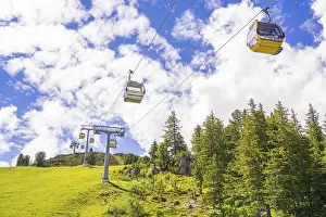 Several cable cars travelling across a green meadow under a cloudy sky