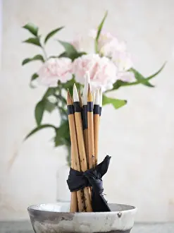 Calligraphy brushes are tied with a black ribbon and placed in a ceramic bowl