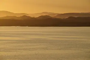 Calm atmosphere over the sea, hills and an orange sunrise