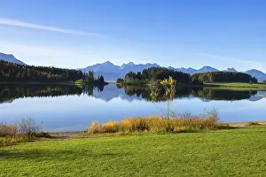 A calm lake reflects the surrounding mountains and forests under a clear sky