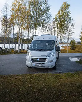 Campervan at resting place in front of autumn birch trees and lake