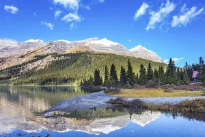 Canada. Rocky Mountains. Sun and mountains are reflected in the smooth water of the lake