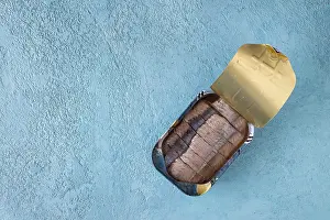 Canned fish, pieces of herring in oil pouring into a jar on a blue background