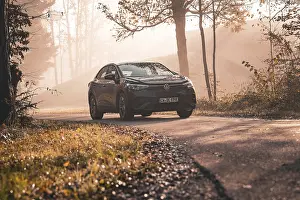 A car drives along a foggy forest path surrounded by autumn trees in the morning