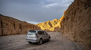 Car driving on a winding road in a gorge while the evening sun illuminates the mountains