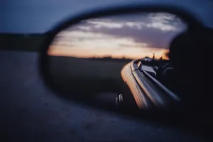 A car mirror reflects a sunset scene during a journey