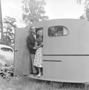 Caravan with owner Sten Hesser and wife, standing in the door. The image can be considered to illustrate the time in the 1950s when people in greater numbers had a car, and with it opportunities to travel and vacation Sweden July. 1953