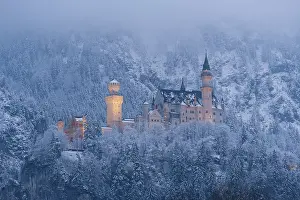 The castle is illuminated and lies in the middle of a snow-covered forest and foggy mountains