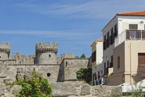 Castle with medieval stone towers next to a Mediterranean building under a blue sky