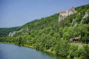 A castle towers over a river in the midst of a green forest and rocks