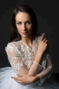 Charming tender young brunette bride in classy delicate white lace gown looking at camera against black background