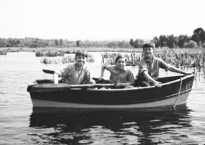 Three cheeky school boys in uniform in rowing boat on lake, something of Lord of the Flies about them! England, UK 1950s - monochrome version