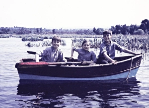 Three cheeky school boys in uniform in rowing boat on lake, something of Lord of the Flies about them! England, UK 1950s - colour version