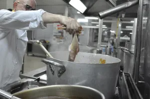 Chef holding fish over a steaming pot in a professional kitchen