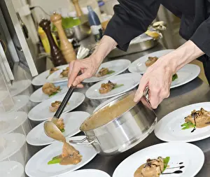 Chef pours sauce over meat pieces on plates