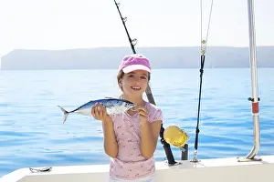 Child little girl fishing in boat holding little tunny tuna fish catch with rod and trolling reels