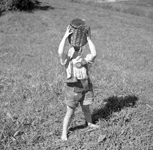 Child stands barefoot in a meadow and drinks water from a wooden-coated vessel