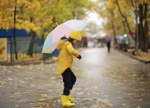 Child in yellow rubber boots and raincoat standing on puddle