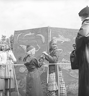 Children in the 1940s. Two girls are catching something in the classic game of fish pond. A string with a clothespin instead of a fishing hook is attached to a stick that is supposed to represent a fishing rod