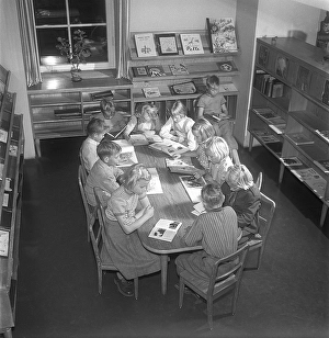 Children of the 1950s. Interior of a public library and a room with bookshelves on the walls. A group of children are sitting at a table, all reading a book each. Sweden 1951 Kristoffersson ref BE25-12