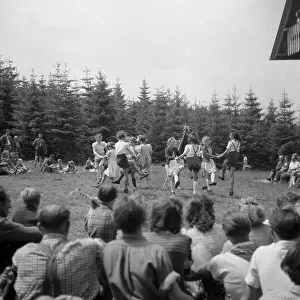 Children dance in a meadow, parents watch them