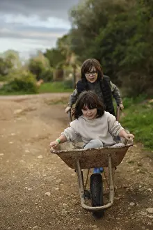Two children enjoying a playful moment with a wheelbarrow on a rural path