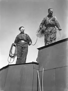 Chimney sweep. Two men works as chimney sweepers and climbing the roof all dressed for work