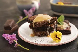 Chocolate brownie with caramel sauce with a cup of coffee on black concrete background