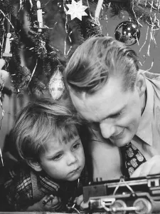 Christmas in the 1940s. A father and son are playing with a toy steam engine by the christmas tree
