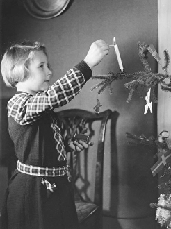 Christmas in the 1940s. A girl is decorating the christmas tree and is lighting a candle in the tree
